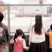 Four children facing away from the camera, looking through a chainlink fence