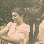 Black and white photograph of a woman in a white dress pruning a rosebush