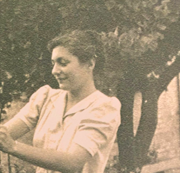 Black and white photograph of a woman in a white dress pruning a rosebush