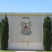 Photo of the side of a building flanked by two juniper trees, in the center of the wall is a depiction of a saint with the word Devotion above