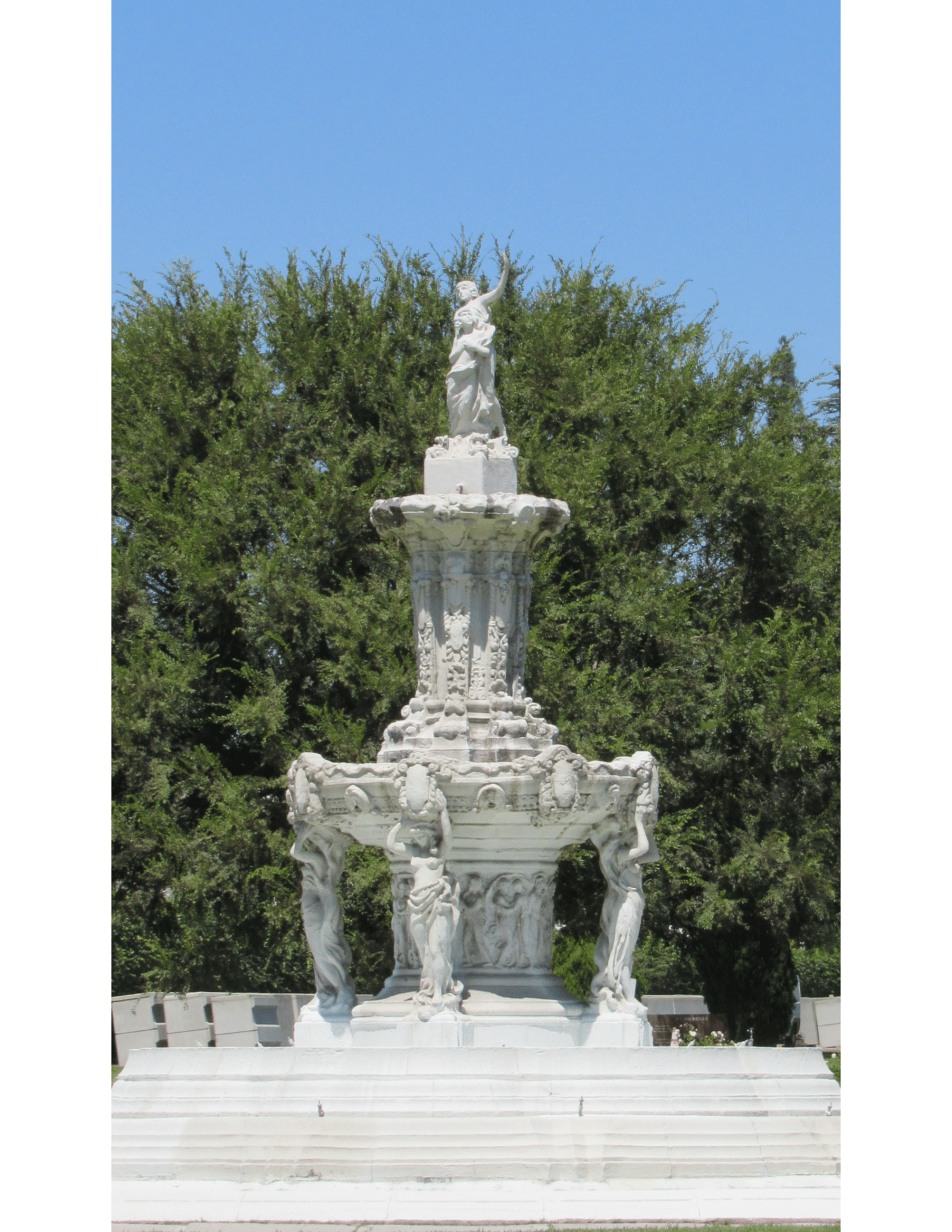 Photograph of a white stone fountain in front of a large tree
