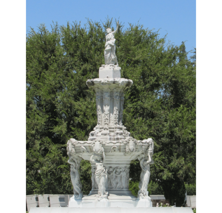Photograph of a white stone fountain in front of a large tree