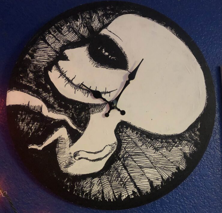 A fetus with an adult head painted in black and white on a clock